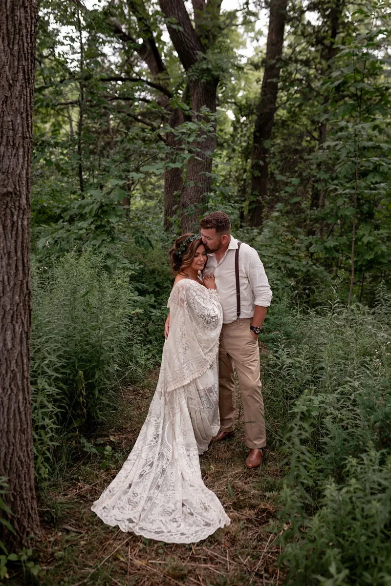 Newlyweds embracing outdoors beneath leafy trees